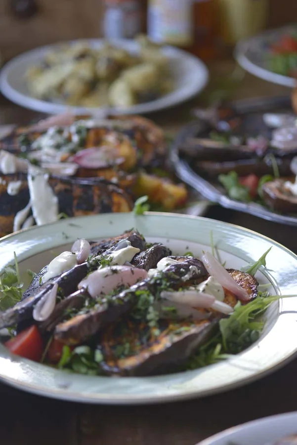 Dishes of grilled vegetables and sliced beef spread across a family dining table