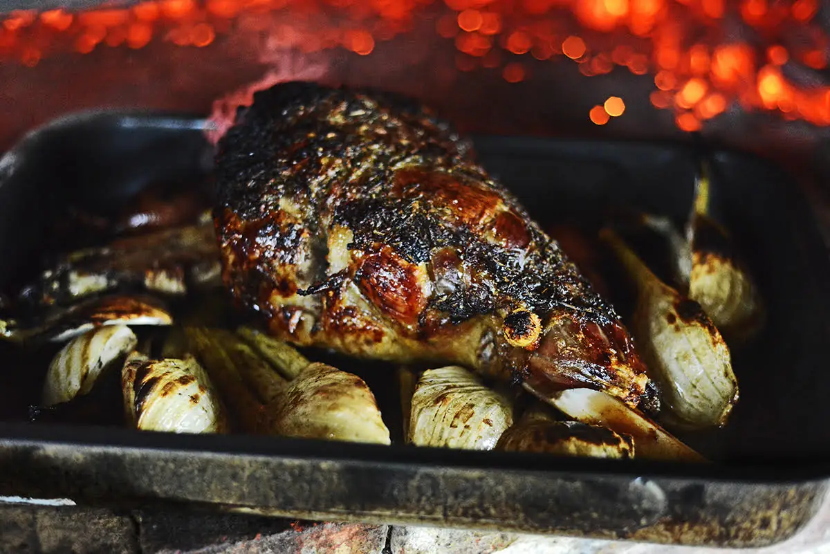 Herb-crusted roast joint with fennel and onions cooking over an open fire