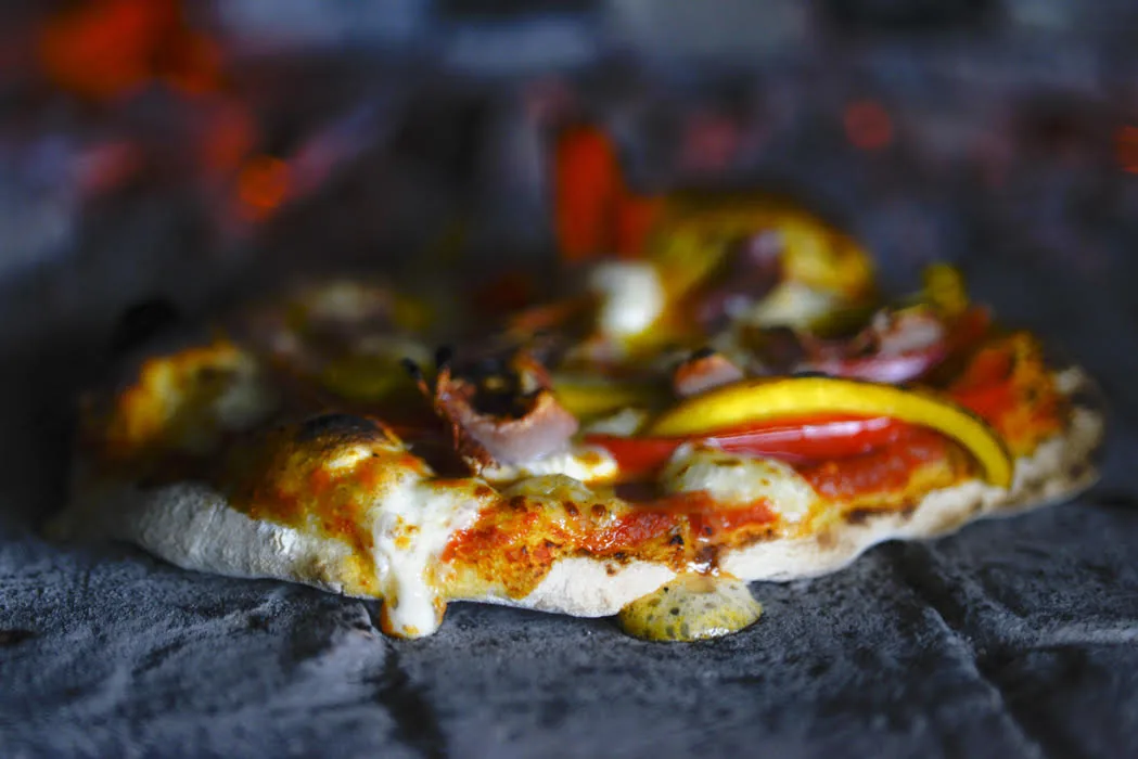Flatbread topped with roasted peppers cooking in a wood-fired oven